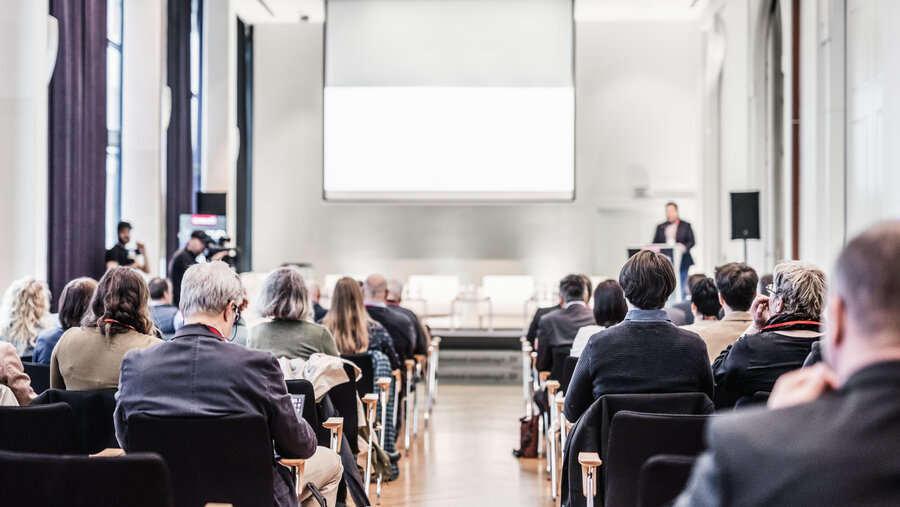Speaker giving a talk in conference hall at business event. Rear view of unrecognizable people in audience at the conference hall. Business and entrepreneurship concept.
